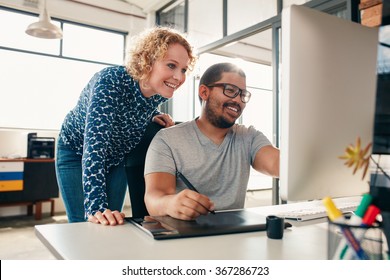 Two young male and female designers working together, with man editing artwork using graphics tablet and a stylus. Creative people coworking on a new project in office. - Powered by Shutterstock