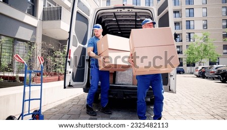 Two Young Male Movers Carrying Cardboard Box From Truck
