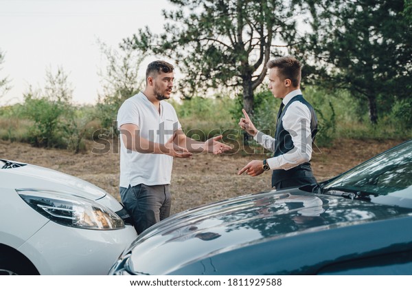two\
Young Man Arguing With Each Other After Car Accident On Street At\
Outdoors. no one wants to give way to each other. Men argue and\
sweat. Two drivers quarreling and gesturing on road\
