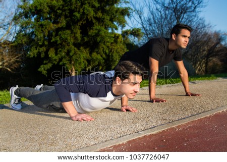 two young man making exercise, making push ups in a city garden.