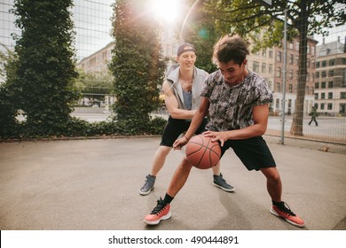 Two young man on basketball court dribbling with ball. Friends playing basketball on court and having fun.