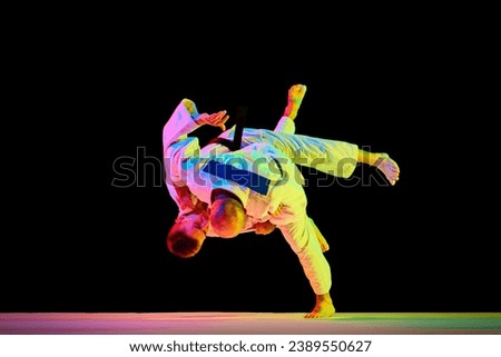 Two young man professional judoist fighting, performing technical skill in neon light isolated black studio background. Concept of martial art, combat sport, health, strength, energy, fit. Copy space