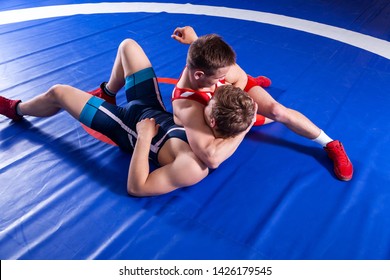 Two young man  wrestlers in red and blue uniform wrestling  on a blue wrestling carpet in the gym. Grappling.