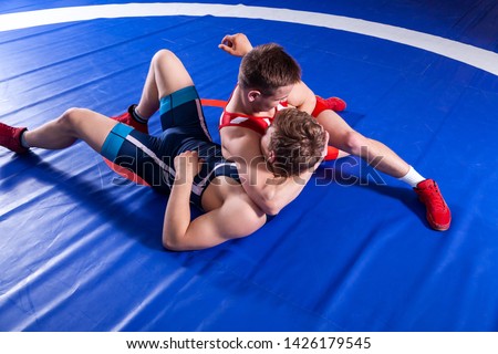 Two young man  wrestlers in red and blue uniform wrestling  on a blue wrestling carpet in the gym. Grappling.