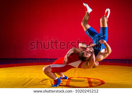 Two young men in blue and red wrestling tights are wrestlng and making a suplex wrestling on a yellow wrestling carpet in the gym, wrestlers doing grapple.