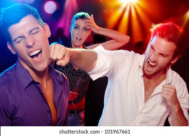 Two Young Men Bopping In The Nightclub For A Woman, Who Is Looking Worried At Background.