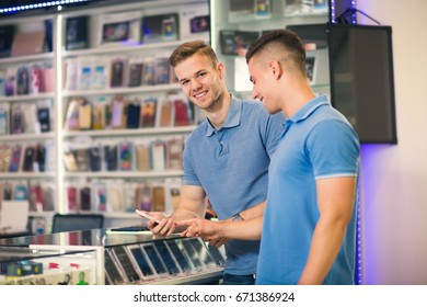 Two Young Men Choosing Smart Phone In The Store Smiling