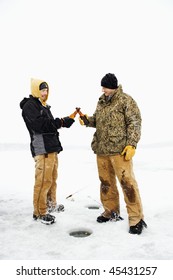 Two Young Men Clink Beers Bottles While Ice Fishing. Vertical Shot.