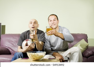 Two Young Men Drinking Beer At Home And Watching Soccer On Tv