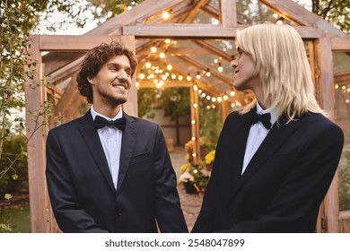 Two young men in formal attire share a joyful moment in a beautifully lit outdoor setting. The enchanting garden is adorned with twinkling lights, creating a romantic atmosphere for their celebration. - Powered by Shutterstock