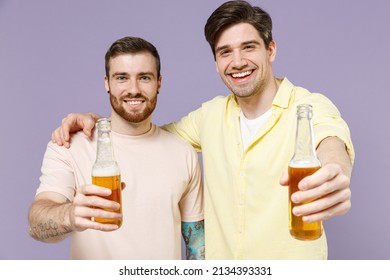 Two young men friends together 20s wearing casual t-shirt hug drink stretch hands with beer bottle to camera isolated on purple background studio portrait People lifestyle concept Tattoo translate fun