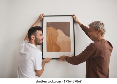 Two Young Men Hanging Picture On Wall