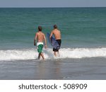 two young men on the beach, going into the ocean.  One has his surf board