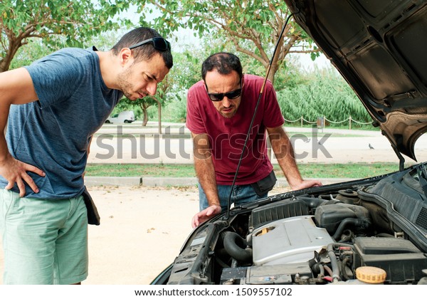 two young men with a problem with the engine of\
a car- insurance