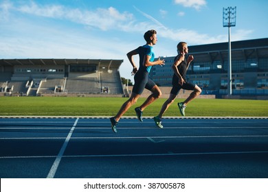 Two Young Men Running On Race Track. Male Professional Athletes Running On Athletics Race Track.