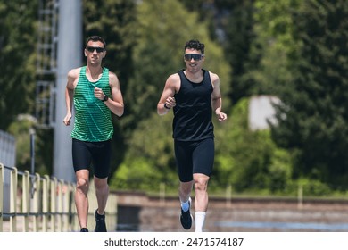 Two young men running in a park, one wearing a green tank top and the other wearing a black tank top - Powered by Shutterstock