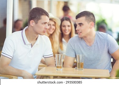 Two young men sitting in a caffe and trying to be cool in front of the girls sitting behind them