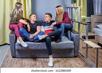 Two Young Men Are Sitting On The Couch In Front Of The TV, The Girls Distract Their Boyfriends From Watching The Movie, They Want To Communicate, And Sit Down Next To The Guys. Double Date In Dorm.