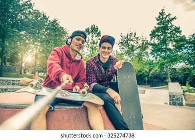 Two young men in a skate park holding a selfie stick and photographing themselves - Two skaters having fun on a skate competition
