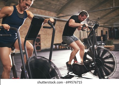 Deux jeunes hommes en vêtements de sport s'asseyant sur des machines à vélo dans la salle de sport et chevauchant rapidement.