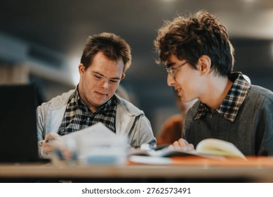 Two young men study together at a table, reviewing papers and books. They collaborate quietly while sharing notes in a focused, supportive learning environment.