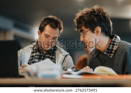 Two young men study together at a table, reviewing papers and books. They collaborate quietly while sharing notes in a focused, supportive learning environment.