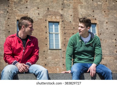 Two Young Men Talking While Sitting On Curb