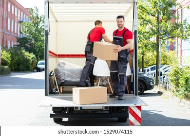 Two Young Men Unloading And Stacking The Brown Cardboard Boxes On Moving Truck