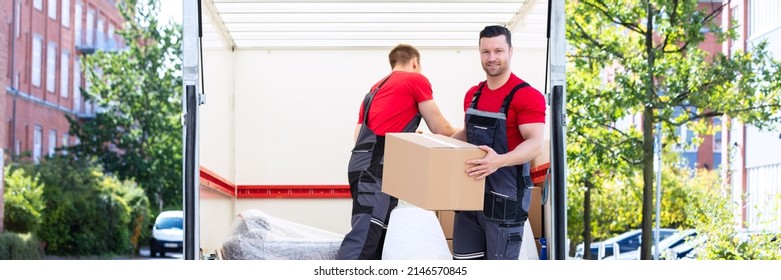 Two Young Men Unloading And Stacking The Brown Cardboard Boxes On Moving Truck