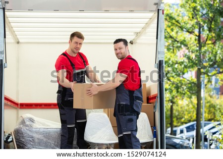 Two Young Men Unloading And Stacking The Brown Cardboard Boxes On Moving Truck