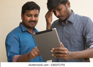 Two Young men using Digital Tablet outside,One was showing the tablet and another person in confusion or due to some mistake he is in confusion. 