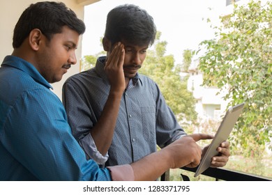 Two Young men using Digital Tablet outside,One was showing the tablet and another person in confusion or due to some mistake he is in confusion.  
