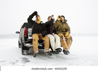 Two Young Men And A Young Woman Drinking Beer While Sitting On The Tailgate Of A Truck In A Winter Environment. Horizontal Shot.