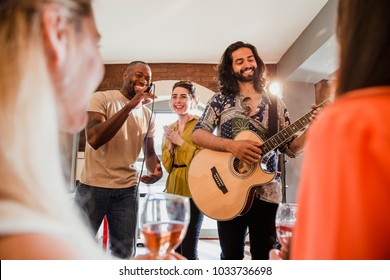 Two Young Men And A Young Woman Are Singing And Playing Guitar At An Entertainment Venue To A Crowd. 