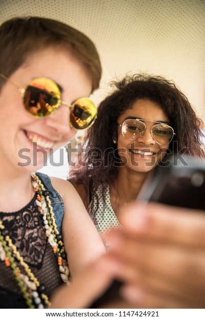 Two young mixed women having\
fun using a smartphone. They look vintage and going vacation in a\
van.