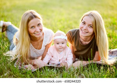 Two Young Mothers Are Walking In The Park In Summer With Her Baby. LGBT Lesbian Couple. The Concept Of  Family And Healthy Lifestyle