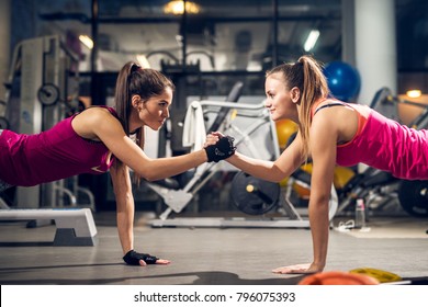 Two young motivated aggressive attractive focused sporty active girls doing push ups and holding hands together while looking each other in the modern gym. - Shutterstock ID 796075393