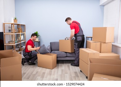 Two Young Movers In Uniform Picking And Putting Products In The Cardboard Boxes