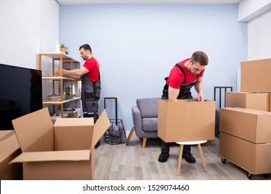 Two Young Movers In Uniform Picking And Putting Products In The Cardboard Boxes