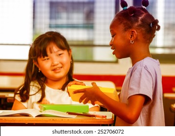 Two young multiracial african asian girls smiling at classroom desk.