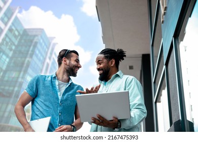 Two Young Multiracial Friends Talk About Start-up Business While Walking In Corporate City District. Brainstorming On Work Break In Front Of Office Building. Copy Space