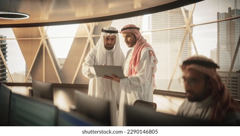 Two Young Muslim Financial Advisers Use Laptop Computer to Discuss a Stock Market Strategy in a Modern Industrial Office. Arab Managers Work in a Banking Research and Development Center