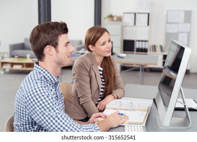 Two Young Office People Looking At The Computer Screen Together On Top Of The Desk.