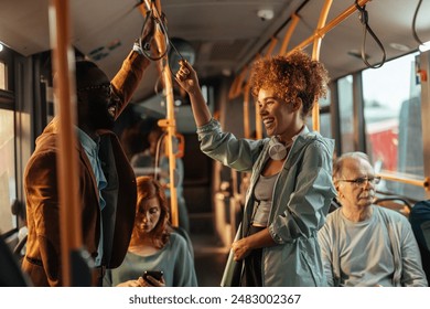 Two young people, a black man and a caucasian girl enjoying a fun conversation while standing on the bus.