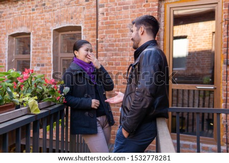 two young people a guy and a girl talking and laugh while standing on the balcony of the old building