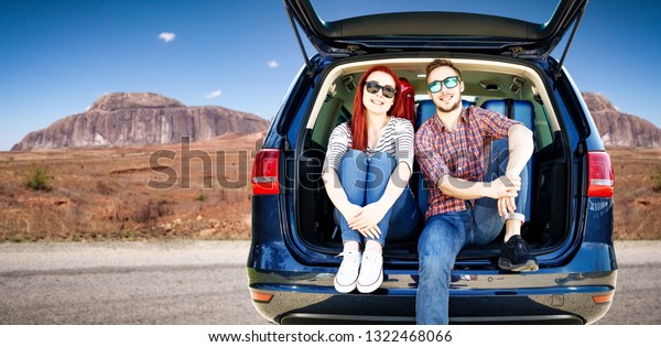 Two young people on summer car trip. Blue big car with\
suitcase. Summer road in the USA. Free place for your decoration.\
Sunny hot day. 