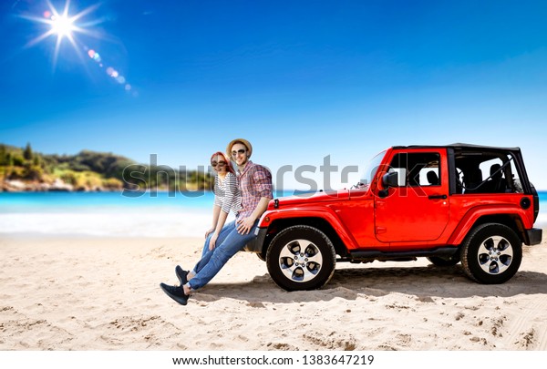 Two young people in red\
summer car on beach. Free space for your decoration. Summer sunny\
day with sun light and blue sky. Small island amd ocean landscape\
