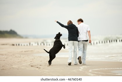 Two Young People Running On The Beach Kissing And Holding Tight With Dog