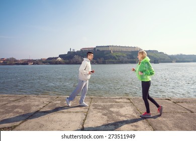 Two Young People Running In Opposite Directions By The Danube River In Novi Sad, Serbia