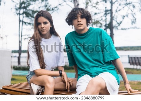 two young people are sitting on a bench in a coastal park